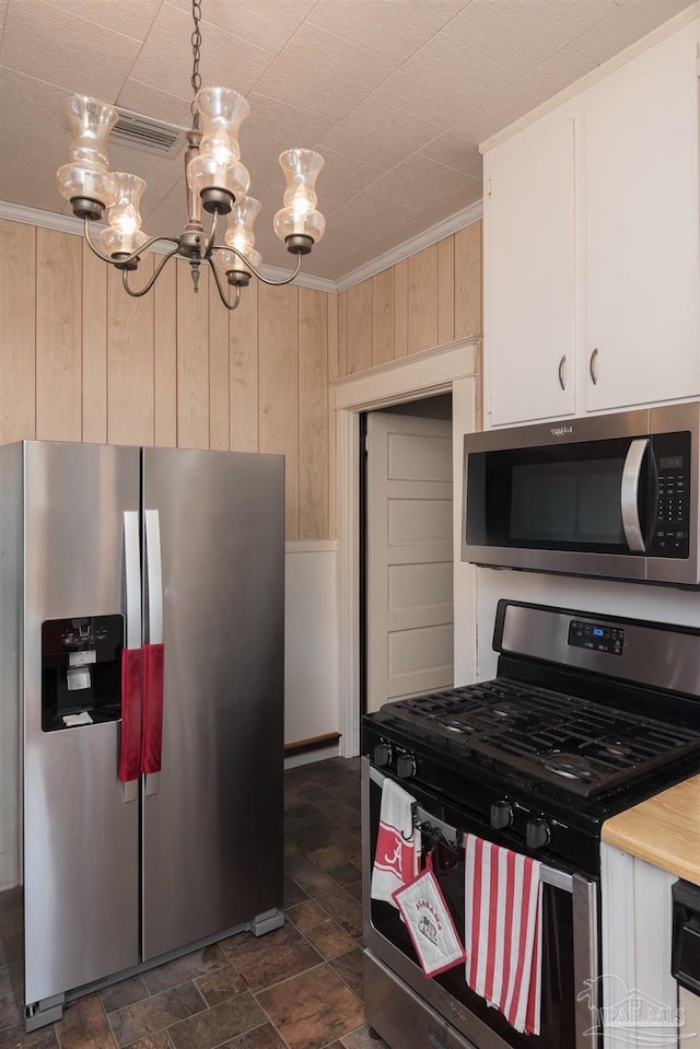 kitchen with appliances with stainless steel finishes, wooden walls, white cabinetry, crown molding, and a chandelier