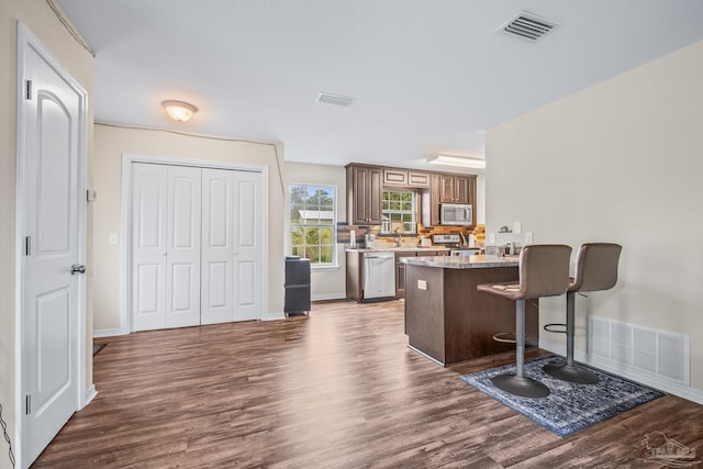 kitchen with appliances with stainless steel finishes, kitchen peninsula, a breakfast bar area, dark hardwood / wood-style flooring, and sink