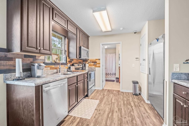 kitchen with sink, dark brown cabinets, backsplash, appliances with stainless steel finishes, and light wood-type flooring