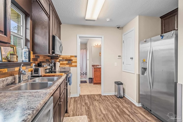 kitchen with sink, tasteful backsplash, a textured ceiling, stainless steel appliances, and light hardwood / wood-style floors