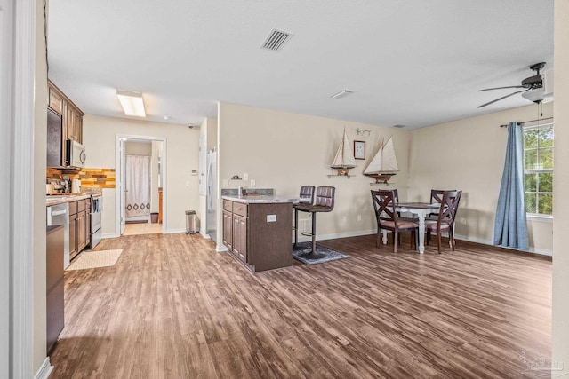 kitchen featuring appliances with stainless steel finishes, a kitchen island, a breakfast bar area, wood-type flooring, and ceiling fan