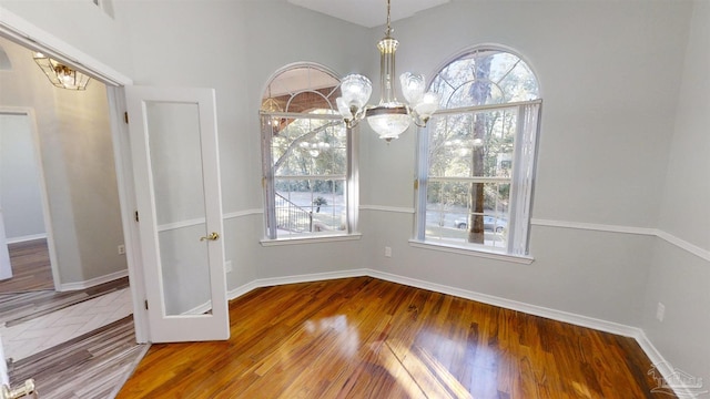 unfurnished dining area with hardwood / wood-style floors and a notable chandelier