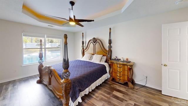 bedroom featuring ceiling fan, dark hardwood / wood-style floors, and a tray ceiling