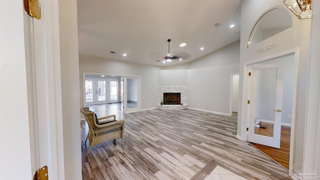 sitting room with ceiling fan, french doors, a stone fireplace, high vaulted ceiling, and light wood-type flooring