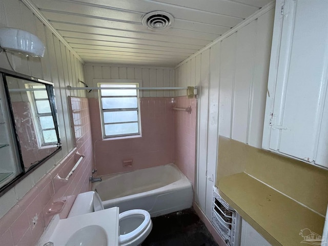 bathroom with tiled shower / bath combo, toilet, and tile walls