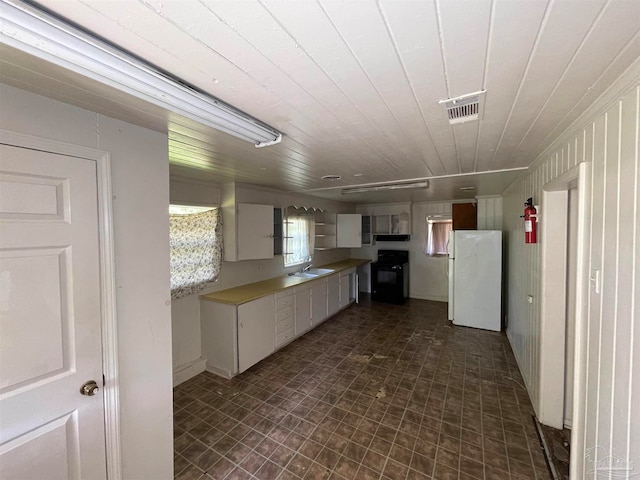 kitchen with white fridge, white cabinets, sink, stove, and dark tile patterned flooring