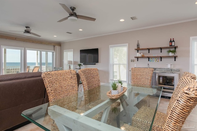 dining room featuring a ceiling fan, wet bar, visible vents, and ornamental molding