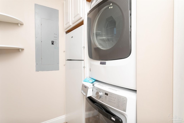 washroom with cabinet space, baseboards, stacked washing maching and dryer, and electric panel