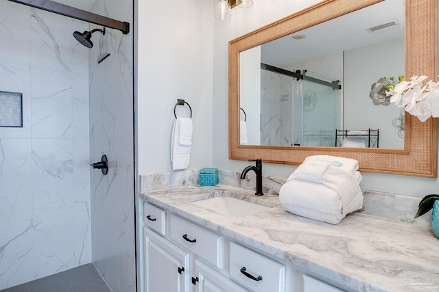full bath with a marble finish shower, vanity, and visible vents
