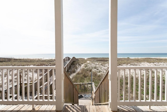 wooden deck featuring a beach view and a water view