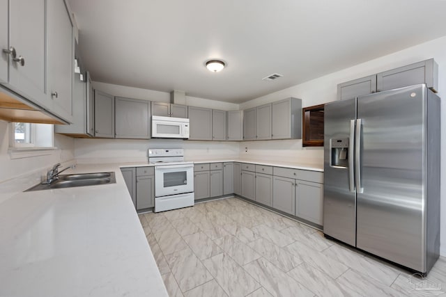 kitchen with marble finish floor, visible vents, gray cabinetry, a sink, and white appliances