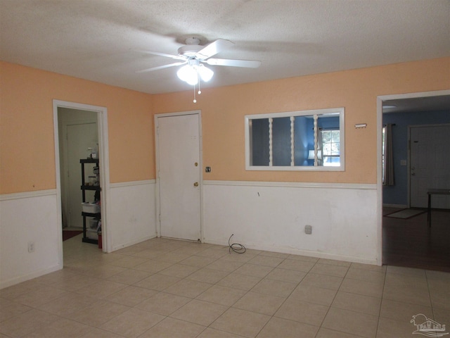 spare room with a textured ceiling, wainscoting, light tile patterned flooring, and a ceiling fan