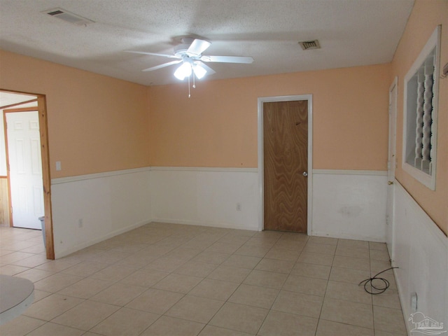 spare room featuring visible vents, wainscoting, ceiling fan, a textured ceiling, and light tile patterned flooring