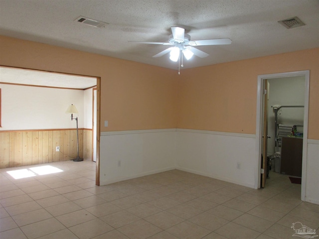 spare room with a wainscoted wall, wooden walls, visible vents, and a textured ceiling