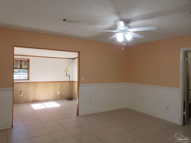 empty room with visible vents, wainscoting, ceiling fan, a textured ceiling, and wood walls