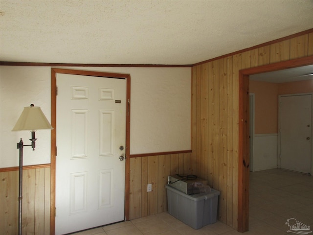 interior space featuring light tile patterned floors, a textured ceiling, wooden walls, a wainscoted wall, and crown molding