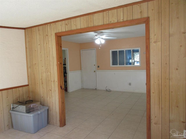 spare room featuring wood walls, ornamental molding, a ceiling fan, and wainscoting