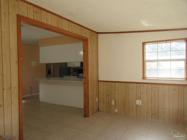 empty room featuring a textured ceiling, ornamental molding, wainscoting, and wooden walls