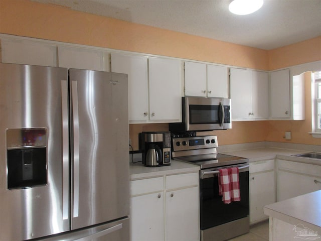 kitchen featuring light tile patterned floors, white cabinets, stainless steel appliances, light countertops, and a sink