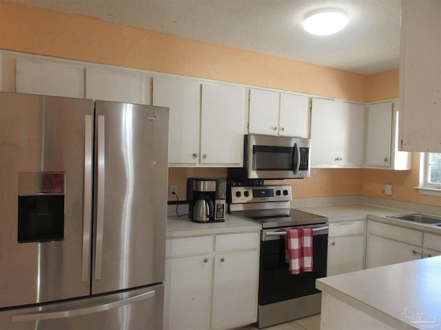 kitchen with light tile patterned flooring, stainless steel appliances, a sink, white cabinetry, and light countertops