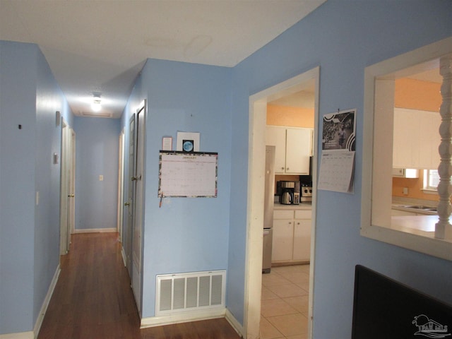 hall featuring baseboards, visible vents, and wood finished floors