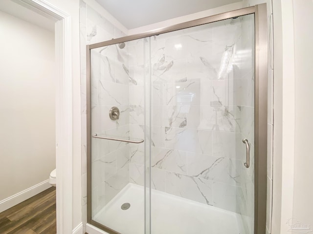 bathroom with hardwood / wood-style floors, a shower with door, and toilet