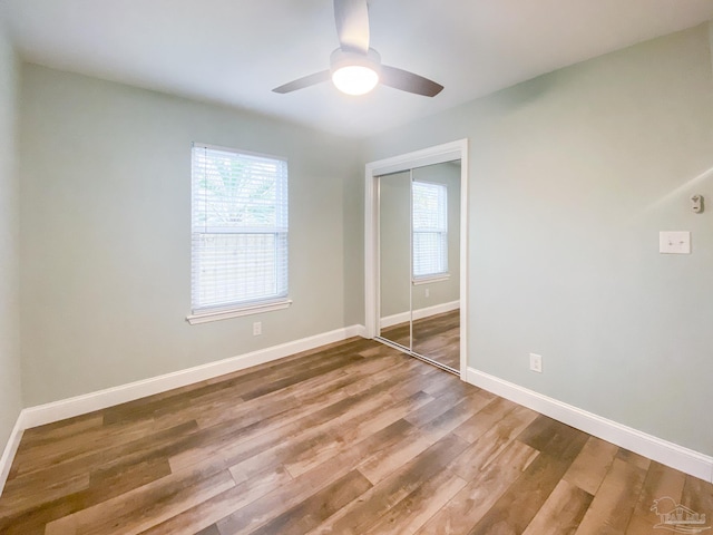 unfurnished bedroom featuring ceiling fan, multiple windows, wood-type flooring, and a closet