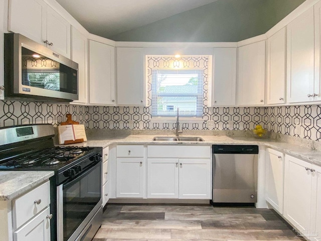 kitchen featuring vaulted ceiling, sink, white cabinets, stainless steel appliances, and light stone countertops