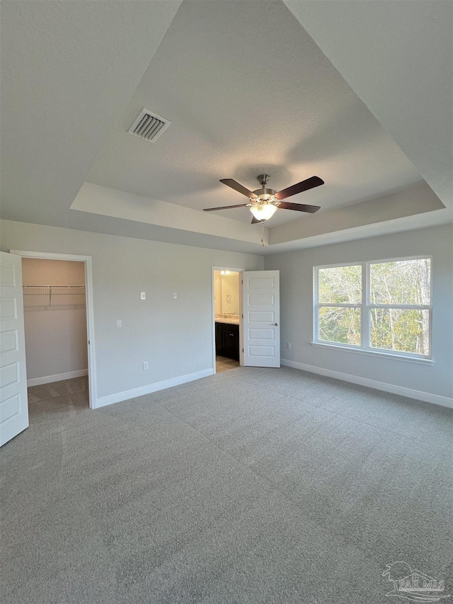 unfurnished bedroom with a walk in closet, a raised ceiling, and carpet flooring