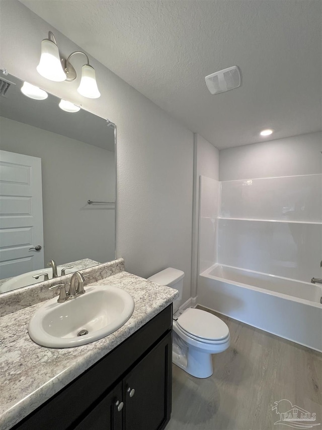 full bathroom with hardwood / wood-style flooring, vanity, a textured ceiling, bathtub / shower combination, and toilet