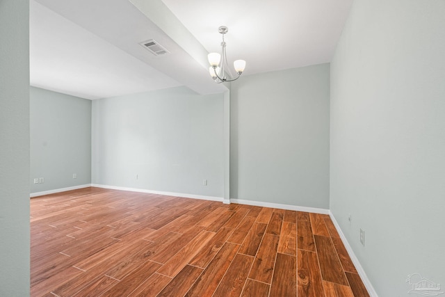 empty room with a notable chandelier, wood finished floors, visible vents, and baseboards