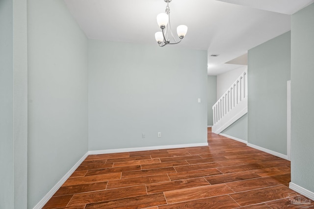 spare room with an inviting chandelier, stairs, baseboards, and wood finished floors
