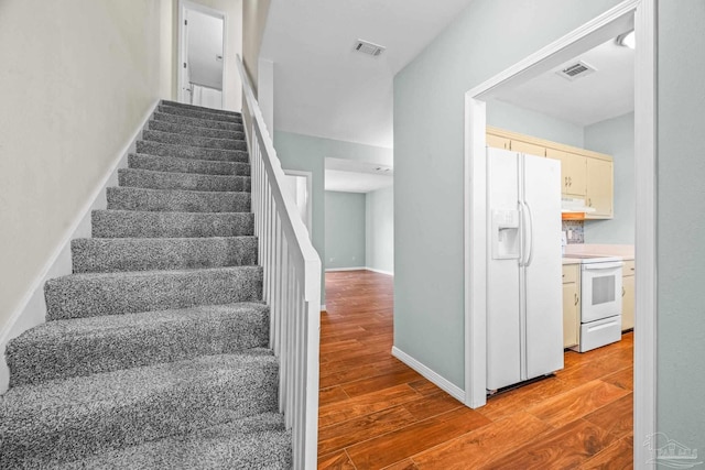 stairs with wood finished floors, visible vents, and baseboards