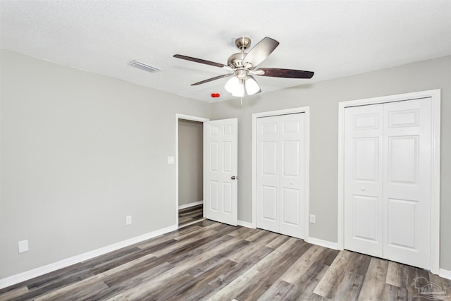 unfurnished bedroom featuring ceiling fan, dark wood-type flooring, a textured ceiling, and two closets