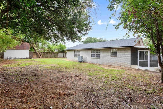 rear view of property with a lawn, a storage shed, cooling unit, and a sunroom