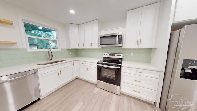 kitchen with a sink, stainless steel appliances, white cabinetry, and light countertops