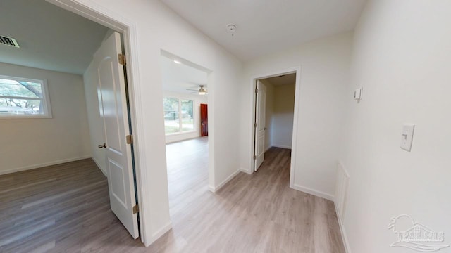 corridor featuring baseboards, light wood-style floors, and a healthy amount of sunlight