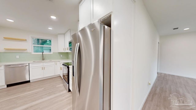 kitchen with light wood finished floors, a sink, white cabinets, appliances with stainless steel finishes, and tasteful backsplash