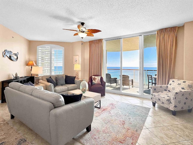 living room with a textured ceiling, a wall of windows, ceiling fan, and a water view