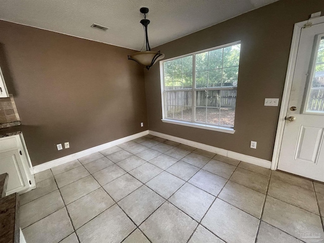 unfurnished dining area featuring a wealth of natural light, light tile patterned flooring, visible vents, and baseboards