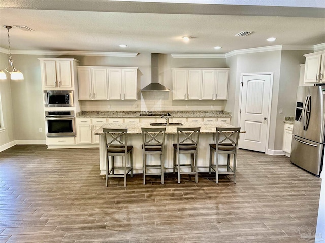 kitchen with visible vents, crown molding, wall chimney exhaust hood, a sink, and stainless steel appliances