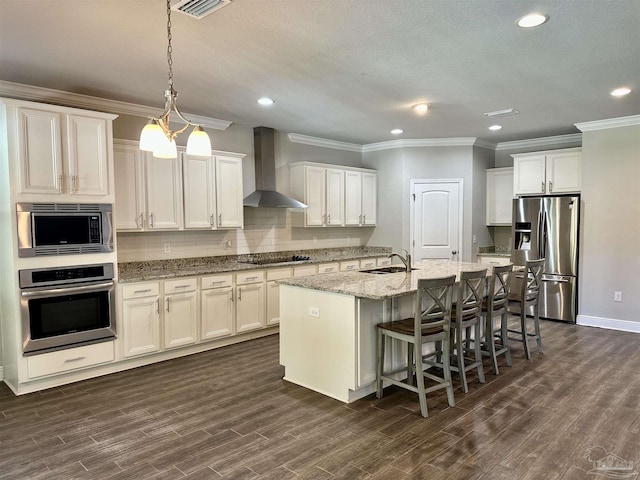 kitchen with wall chimney range hood, appliances with stainless steel finishes, ornamental molding, and a sink