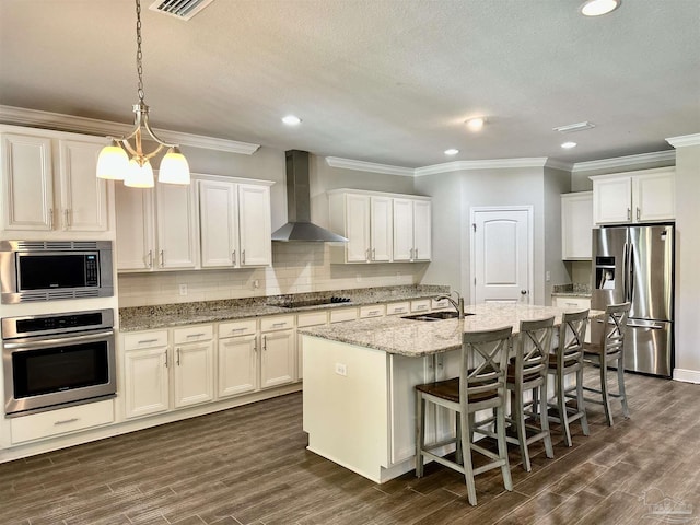 kitchen with appliances with stainless steel finishes, a sink, wall chimney exhaust hood, decorative backsplash, and ornamental molding