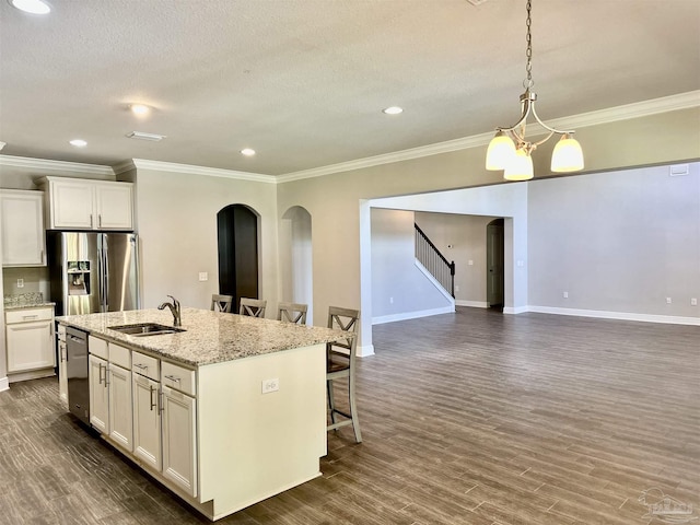 kitchen with appliances with stainless steel finishes, a sink, arched walkways, a kitchen breakfast bar, and ornamental molding