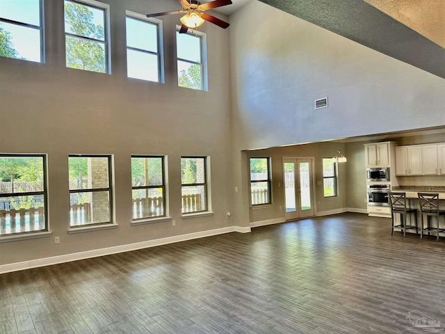 unfurnished living room with a towering ceiling, a wealth of natural light, a ceiling fan, and visible vents