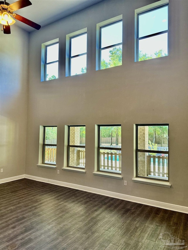 empty room featuring baseboards, a ceiling fan, dark wood-style flooring, and a towering ceiling