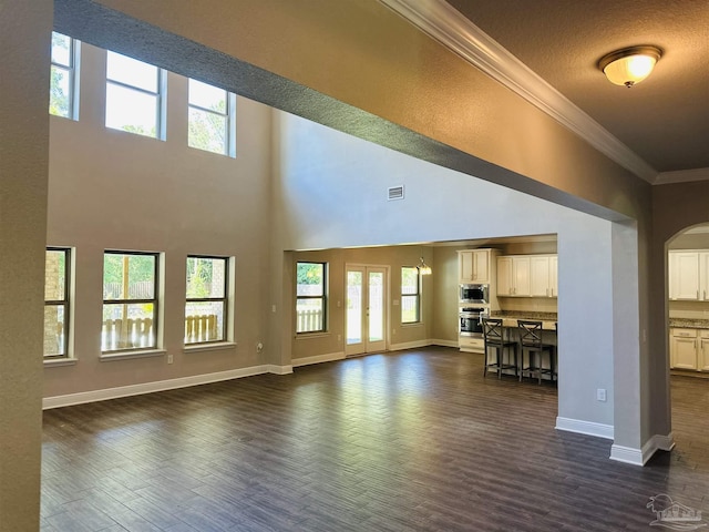 unfurnished living room featuring baseboards, dark wood finished floors, ornamental molding, and a healthy amount of sunlight