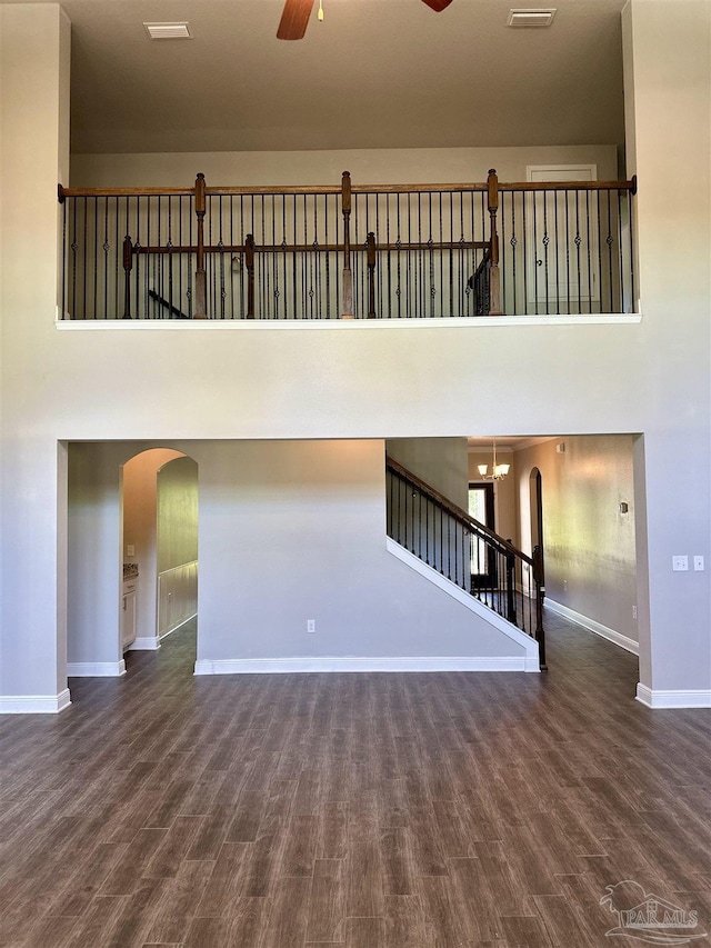 unfurnished living room with arched walkways, ceiling fan, baseboards, and wood finished floors