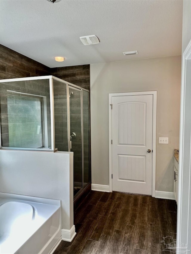 bathroom with wood finished floors, a textured ceiling, baseboards, and a stall shower