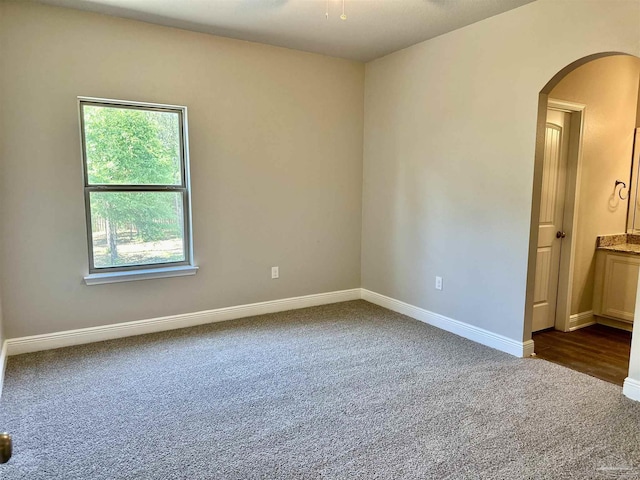spare room with dark carpet, arched walkways, and baseboards